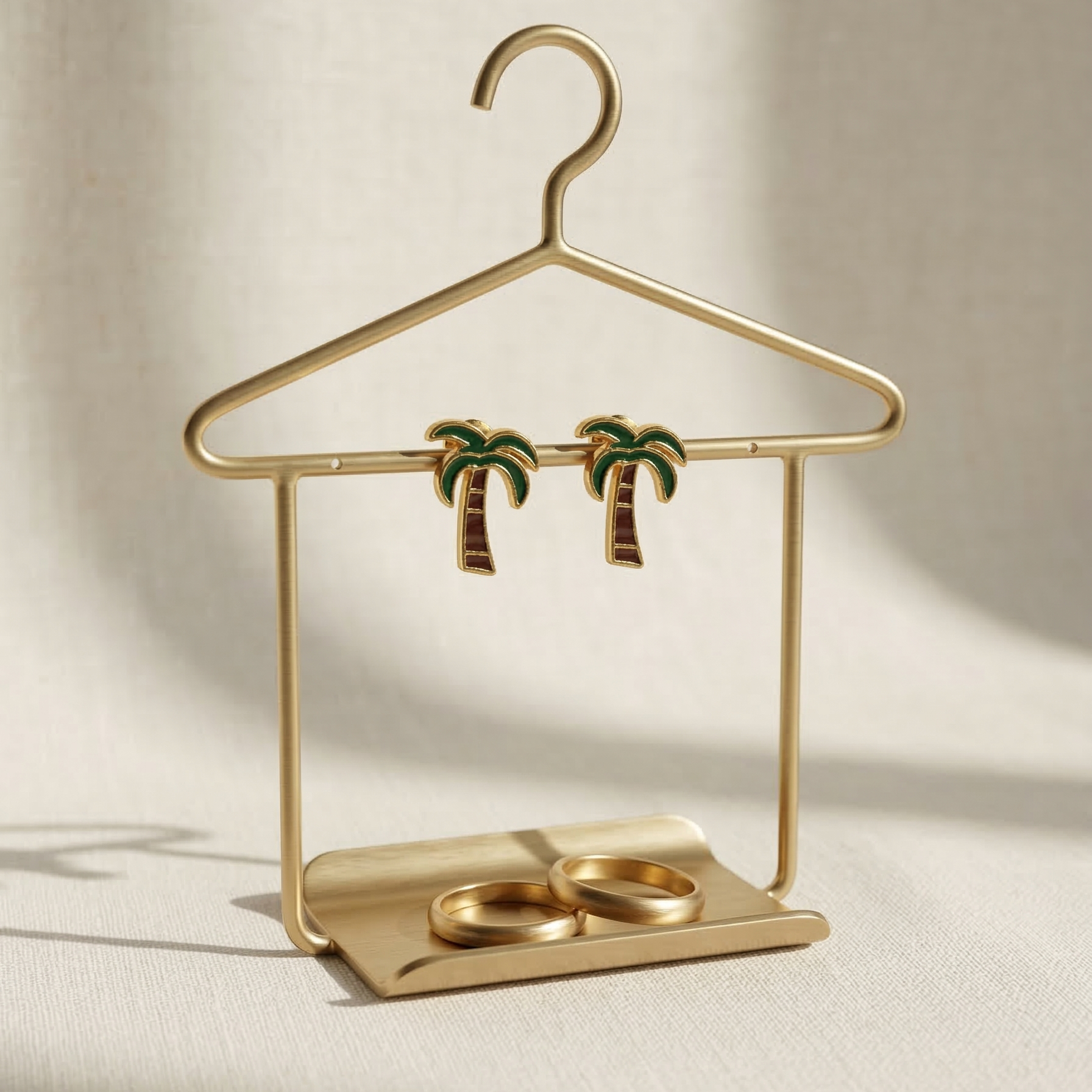 Gold jewelry stand with palm tree earrings on a beige background