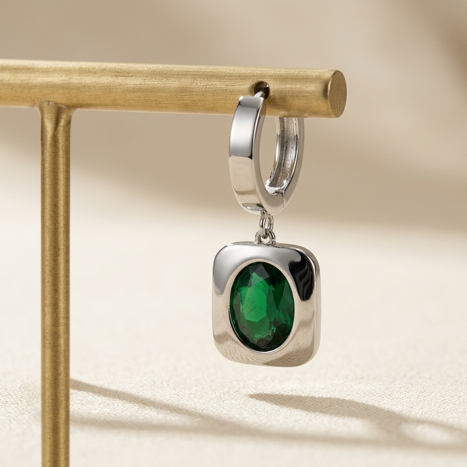 Silver earring with a green gemstone on a beige background
