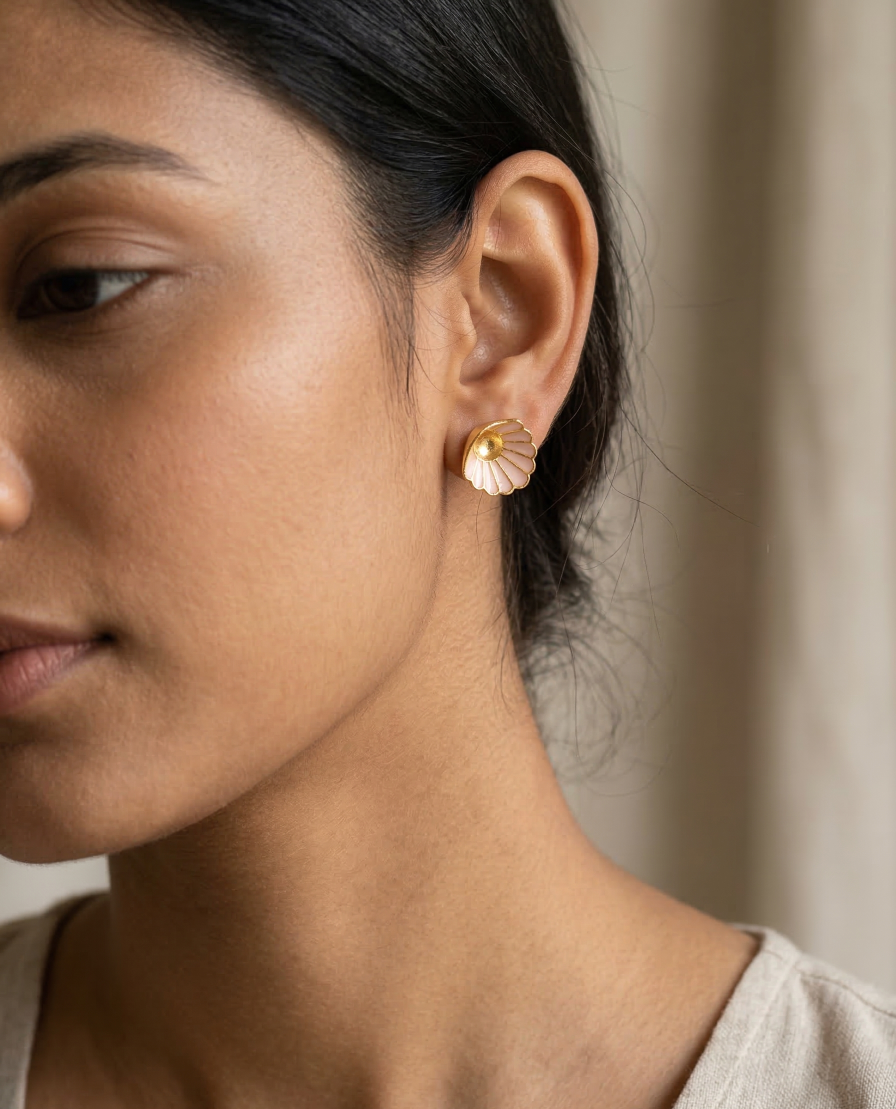 Close-up of a person wearing gold earrings with a neutral background