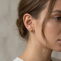 Close-up of a person wearing a gold heart-shaped earring against a neutral background