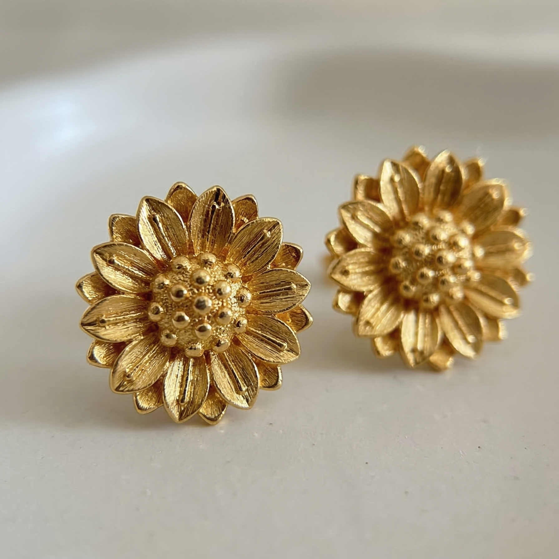 Gold sunflower-shaped earrings on a white background