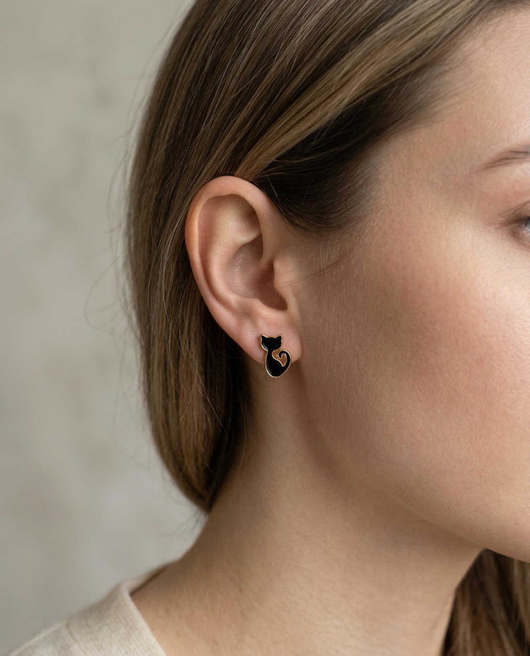 Close-up of a person wearing a black cat-shaped earring against a neutral background