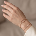 Hand wearing a delicate rose gold bracelet on a neutral background