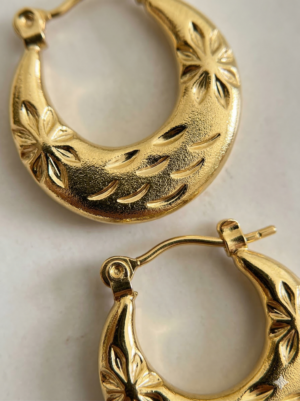 Gold hoop earrings with intricate designs on a light background