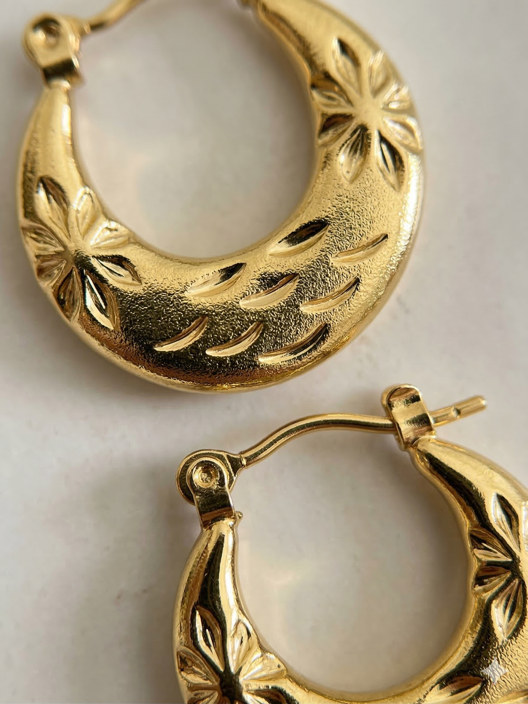 Gold hoop earrings with intricate designs on a light background