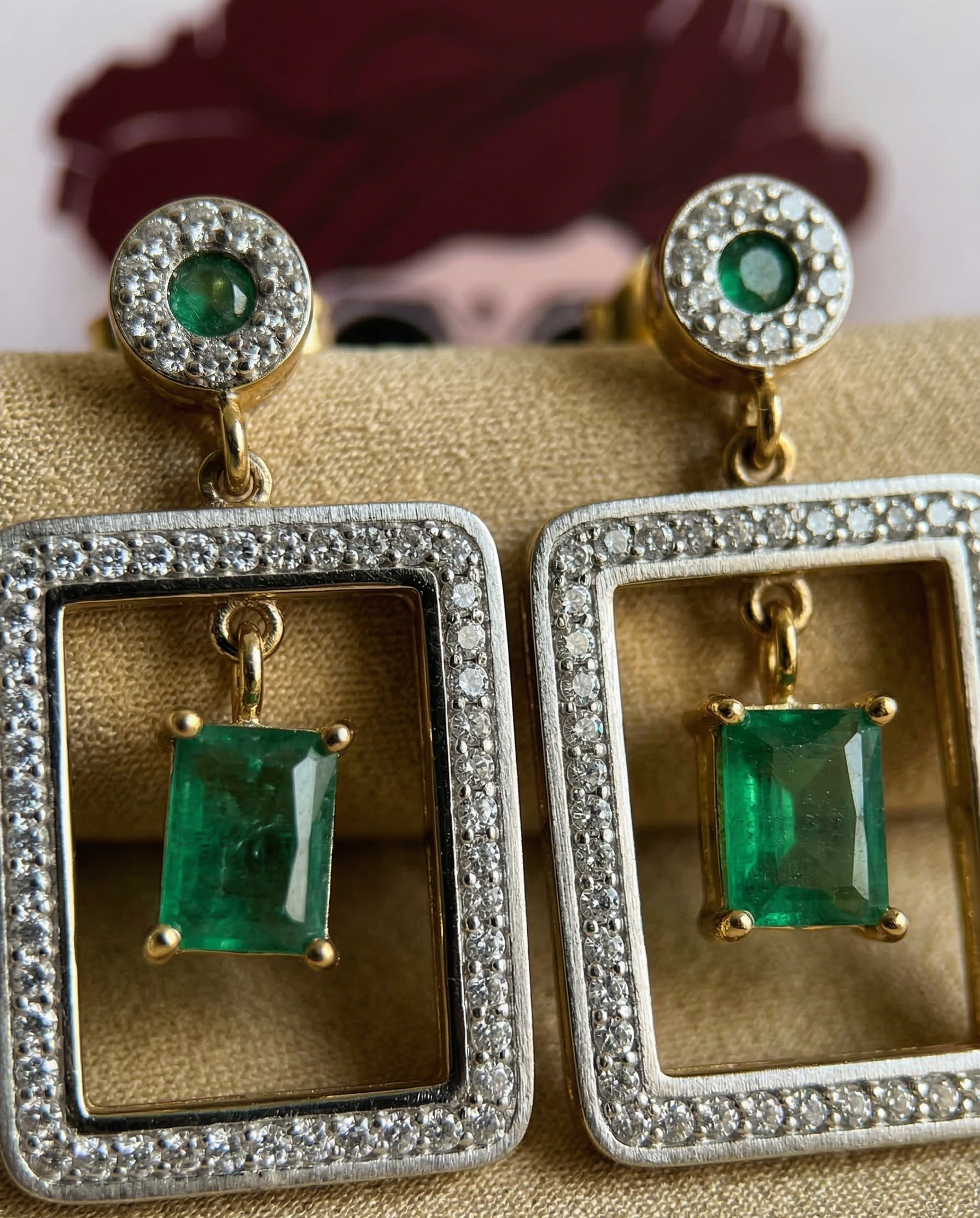 Pair of emerald and diamond earrings on a gold display stand.