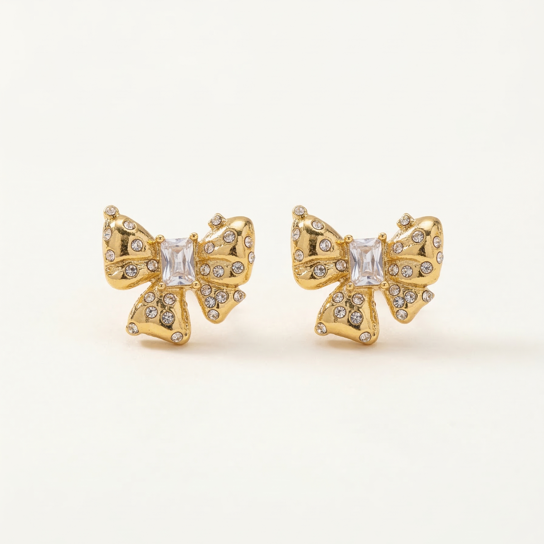 Gold butterfly earrings with clear gemstones on a light beige background