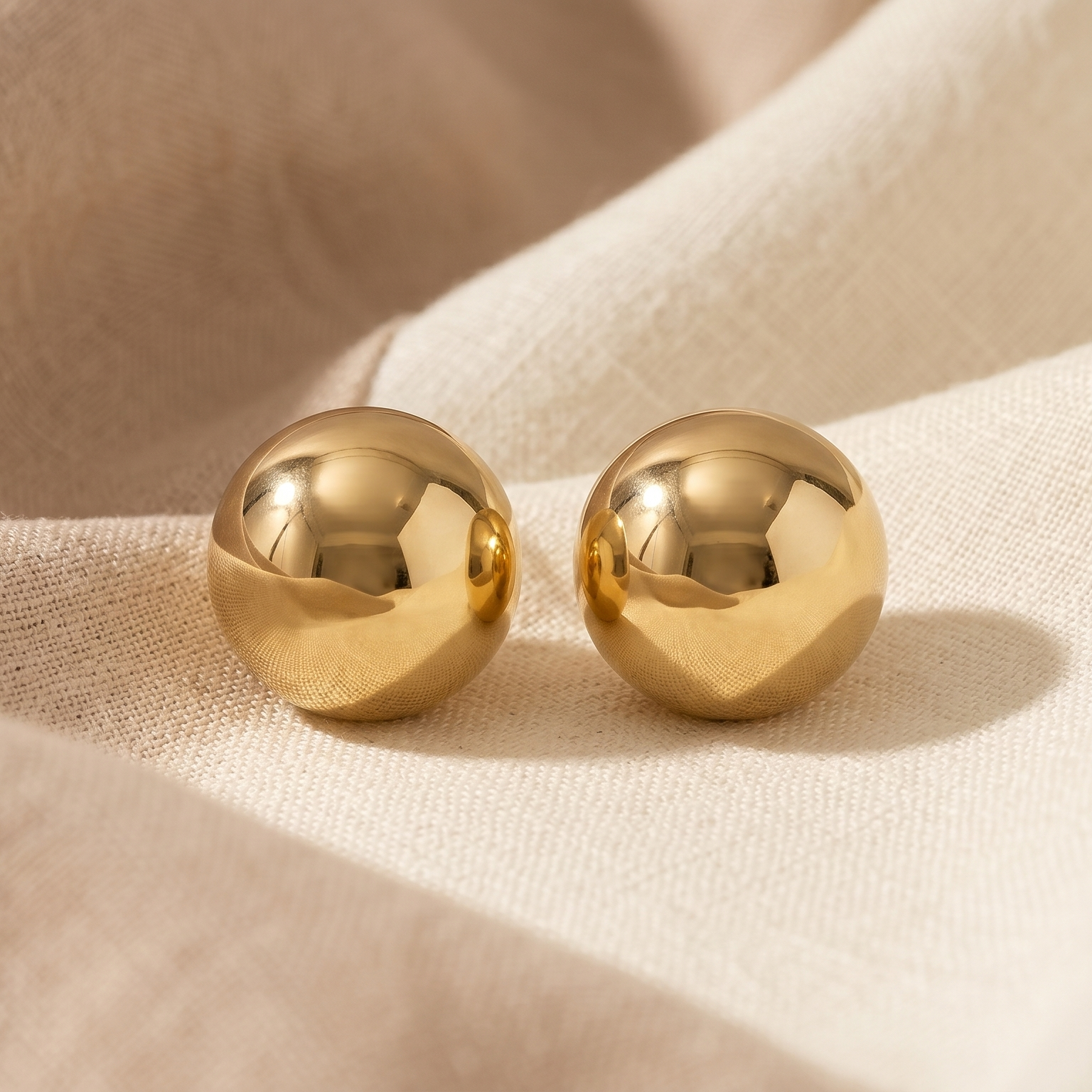 Pair of gold spherical earrings on beige fabric