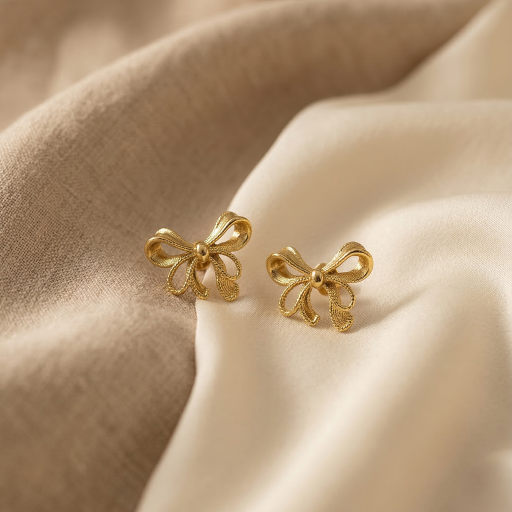 Gold bow-shaped earrings on beige fabric