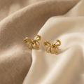 Gold bow-shaped earrings on beige fabric