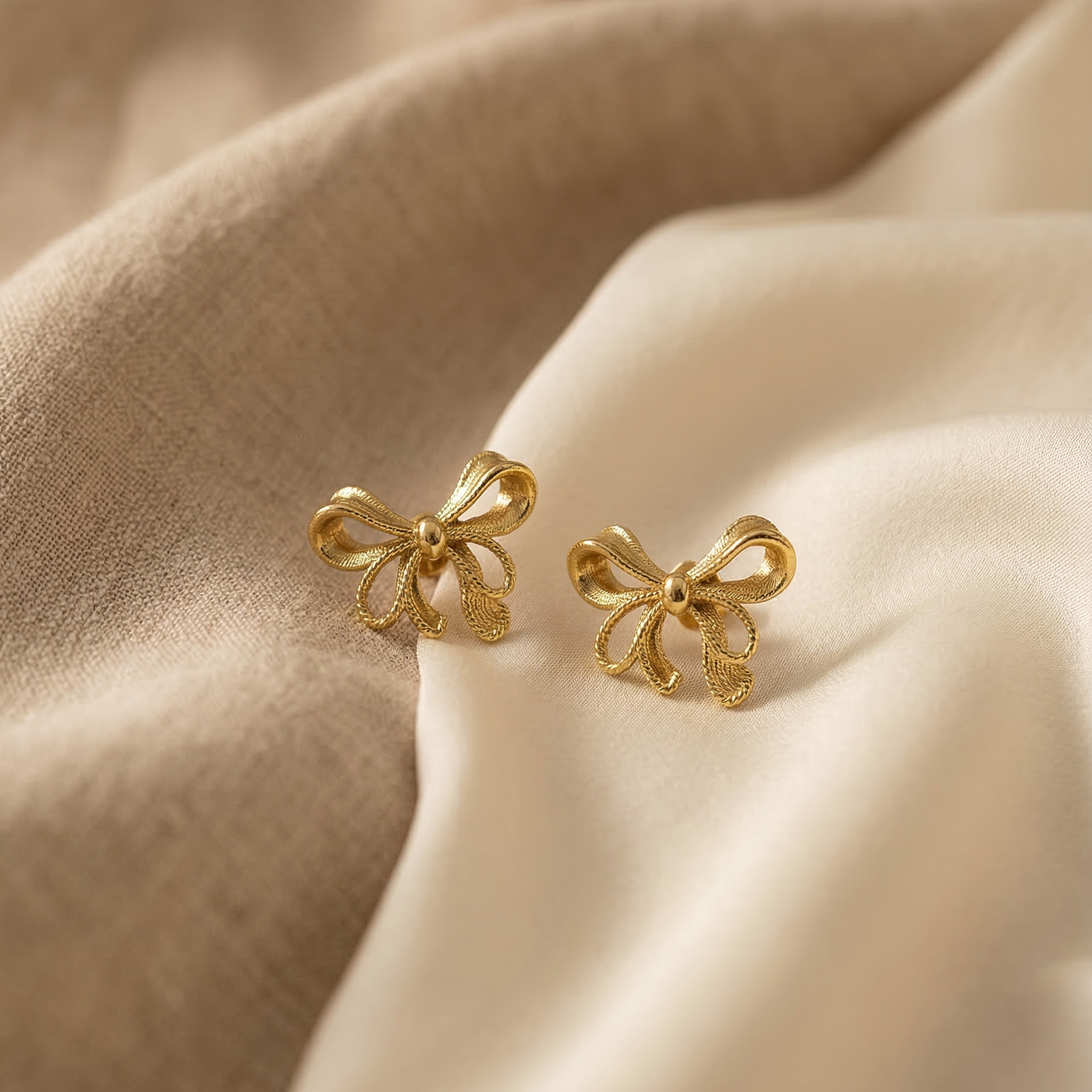 Gold bow-shaped earrings on beige fabric