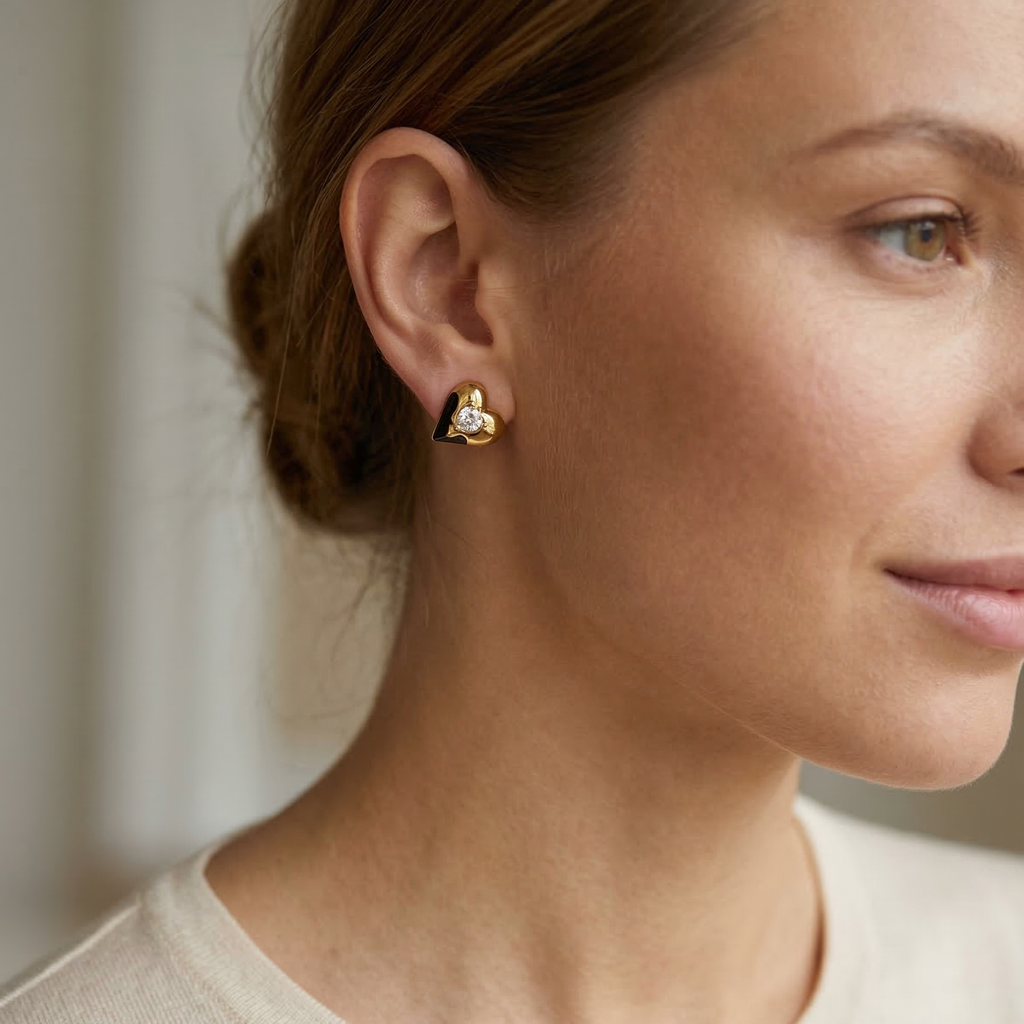 Close-up of a woman wearing gold heart-shaped earrings with a neutral background