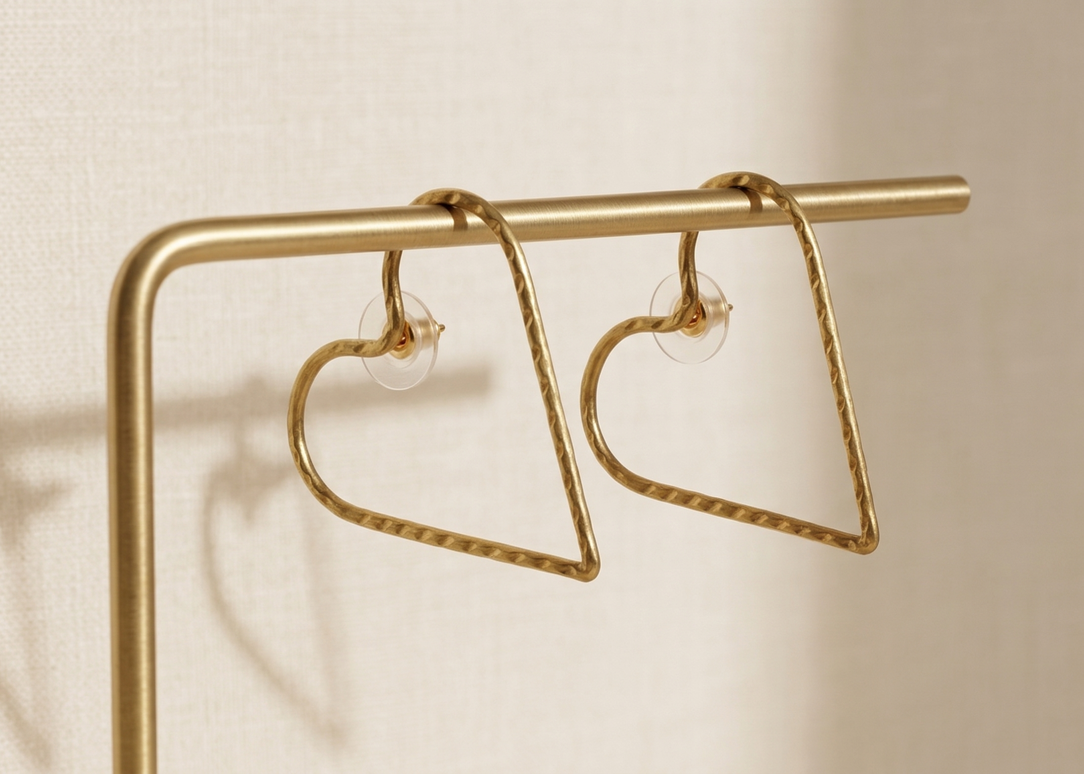 Gold heart-shaped earrings on a stand against a beige background