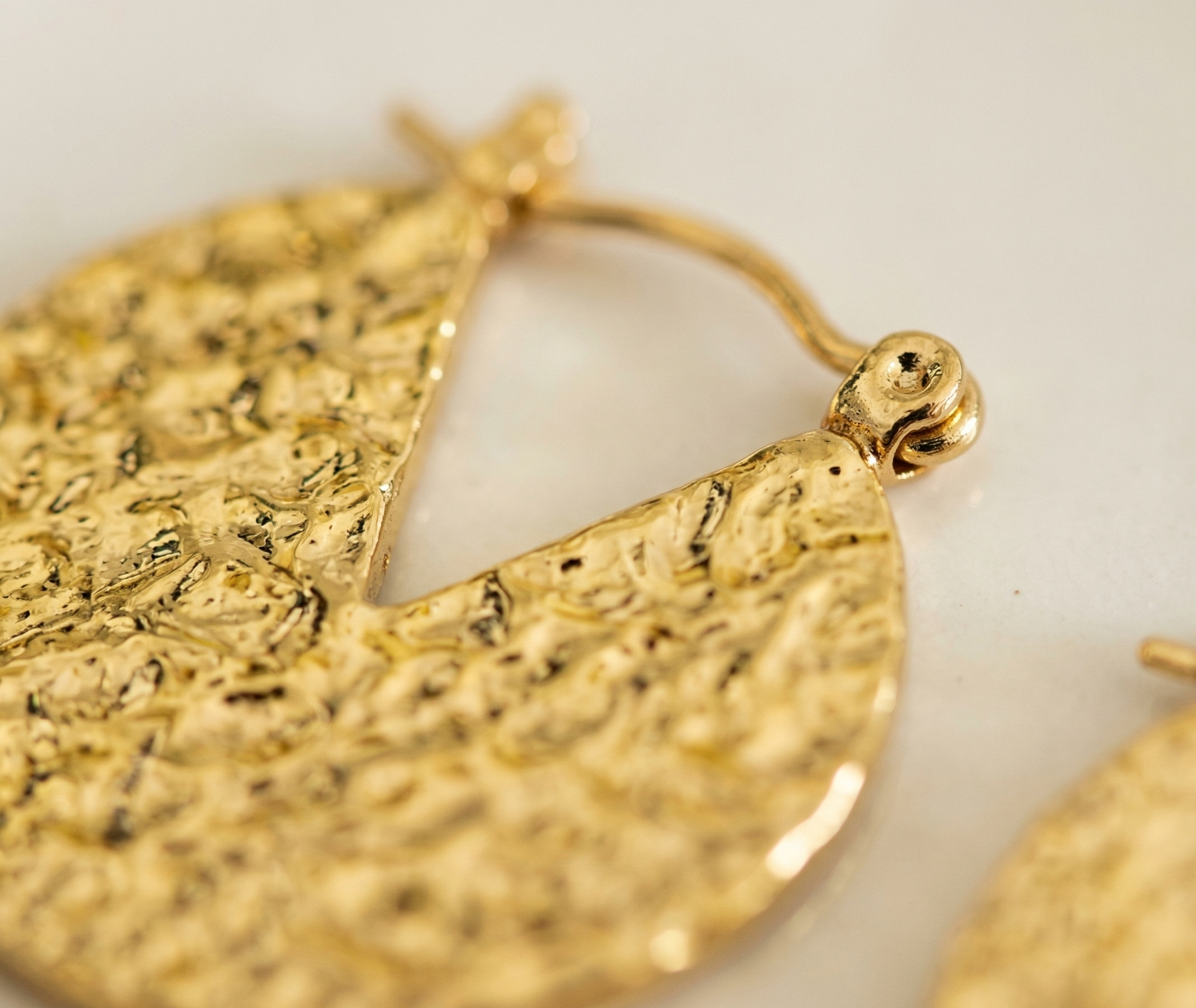 Gold hoop earrings with textured design on a light background