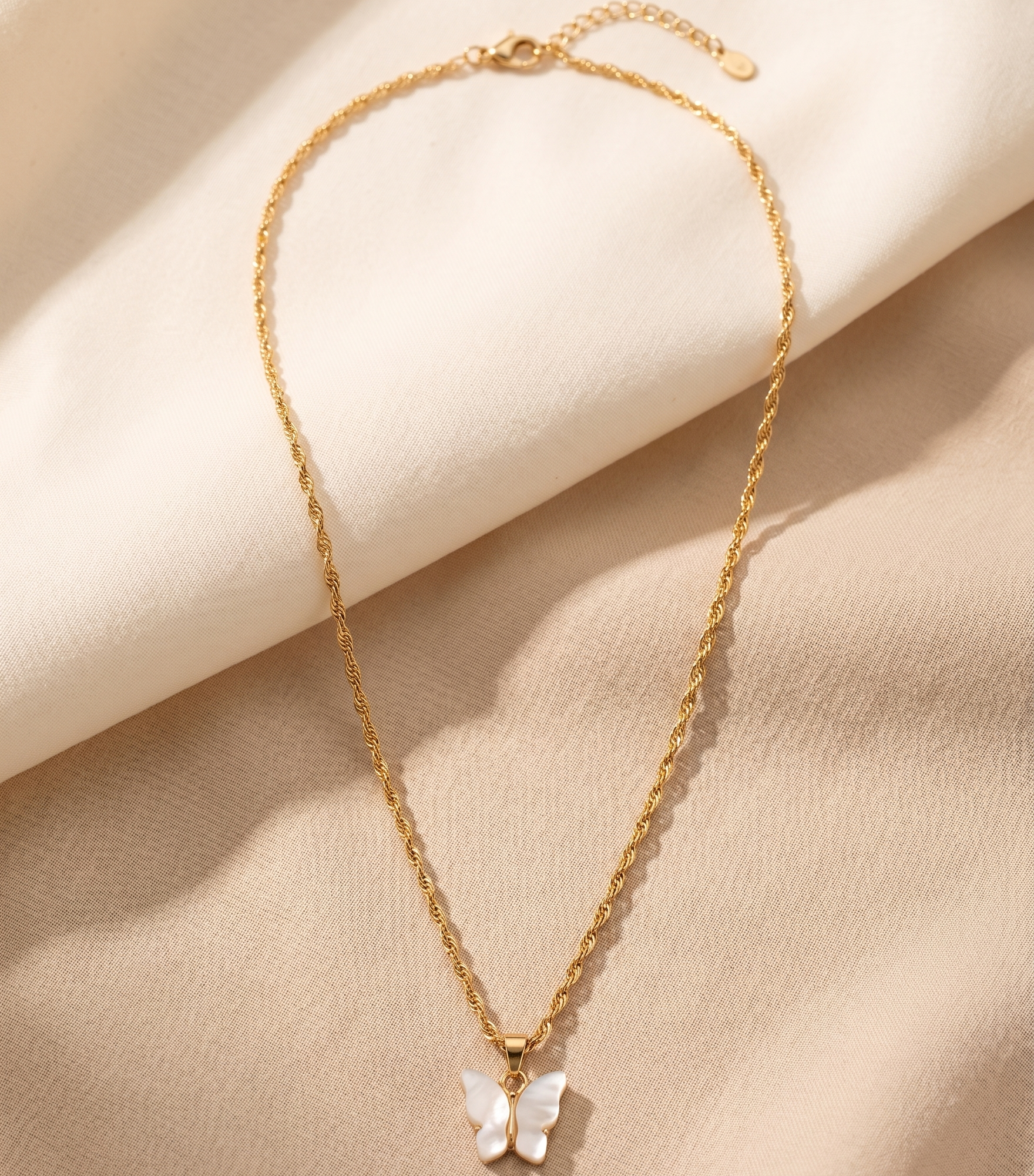Gold necklace with a butterfly pendant on a beige fabric background