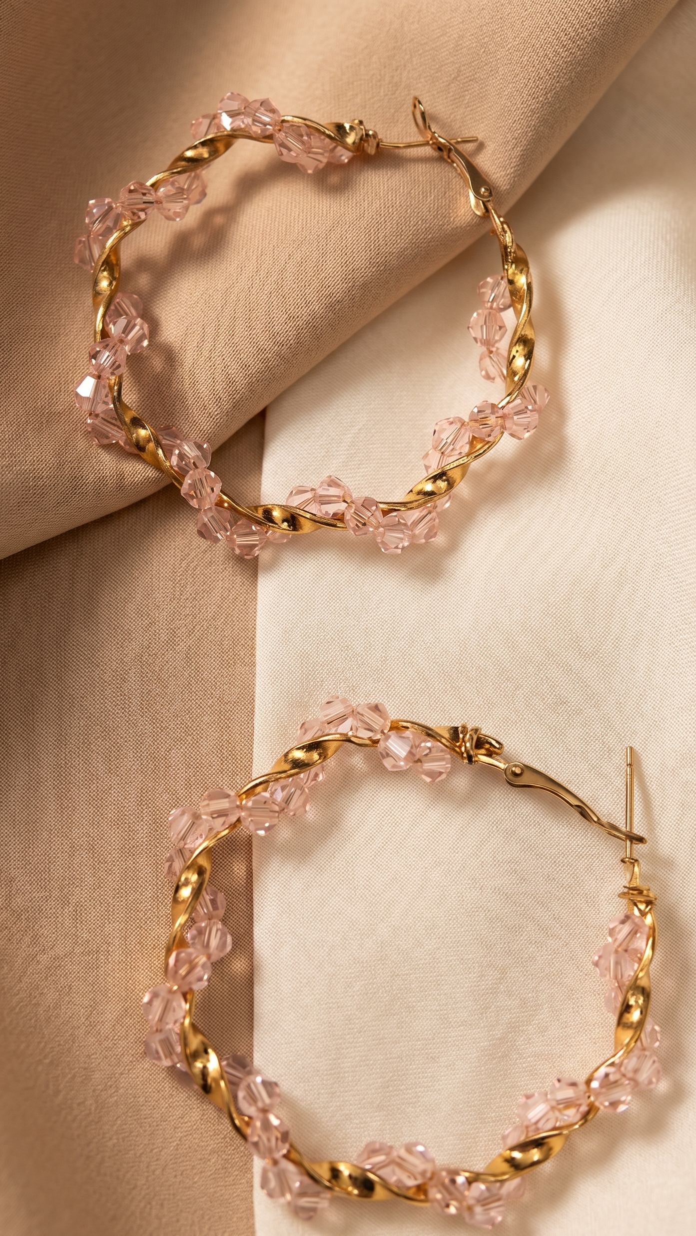 Gold hoop earrings with pink gemstones on a beige fabric background