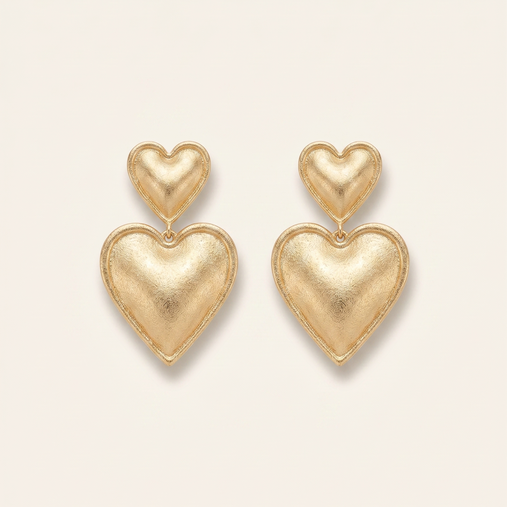 Gold heart-shaped earrings on a light beige background