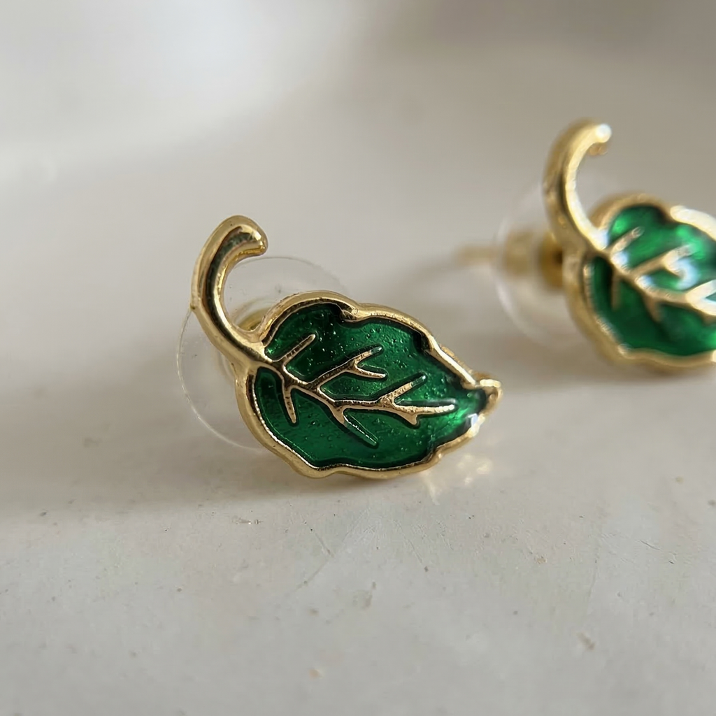 Gold and green leaf-shaped earrings on a light background