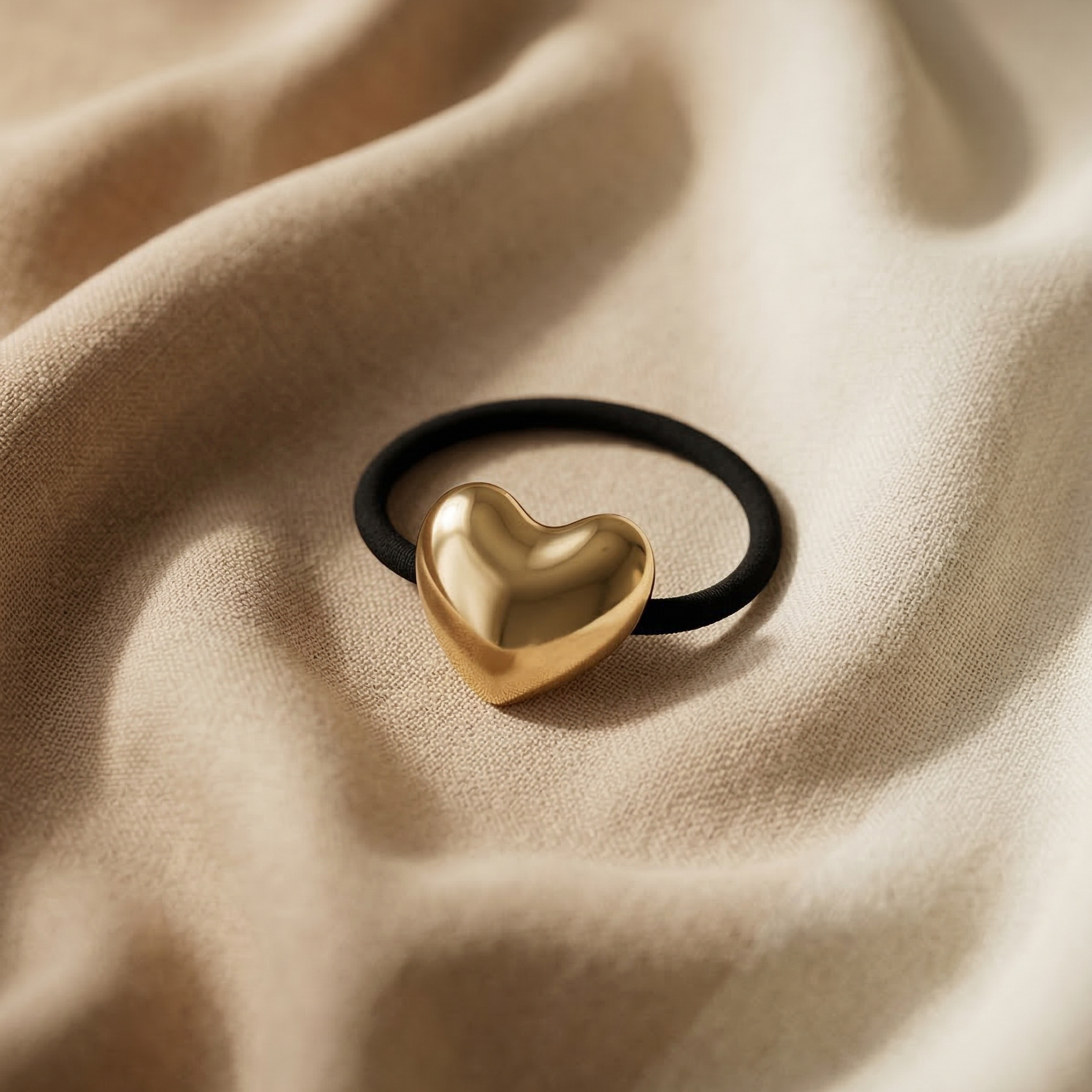 Gold heart-shaped hair tie on a beige fabric background