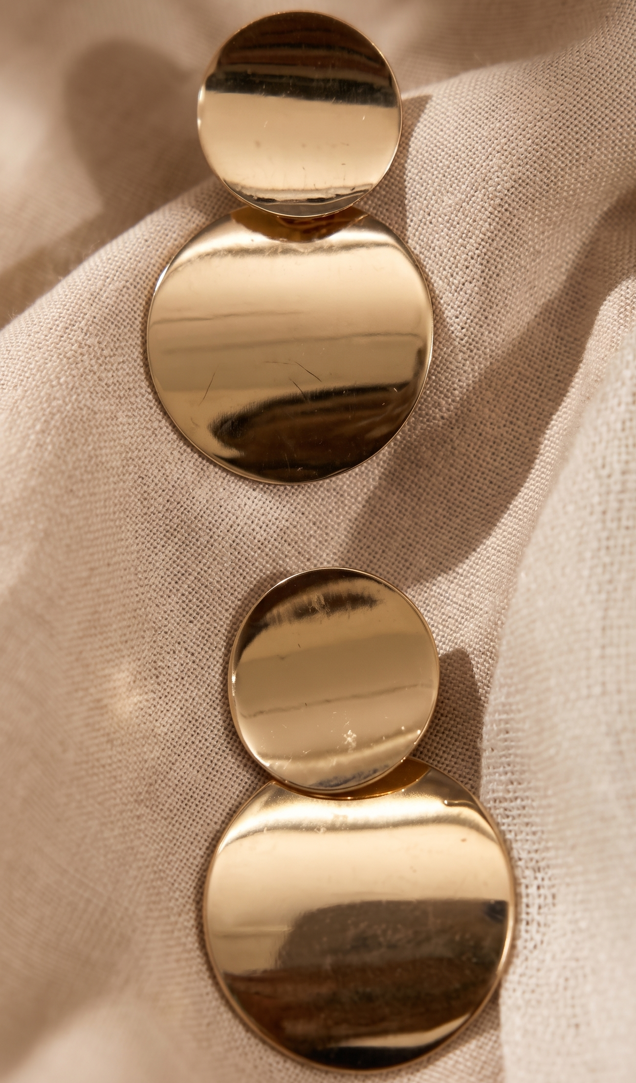 Gold earrings with three round discs on a beige fabric background