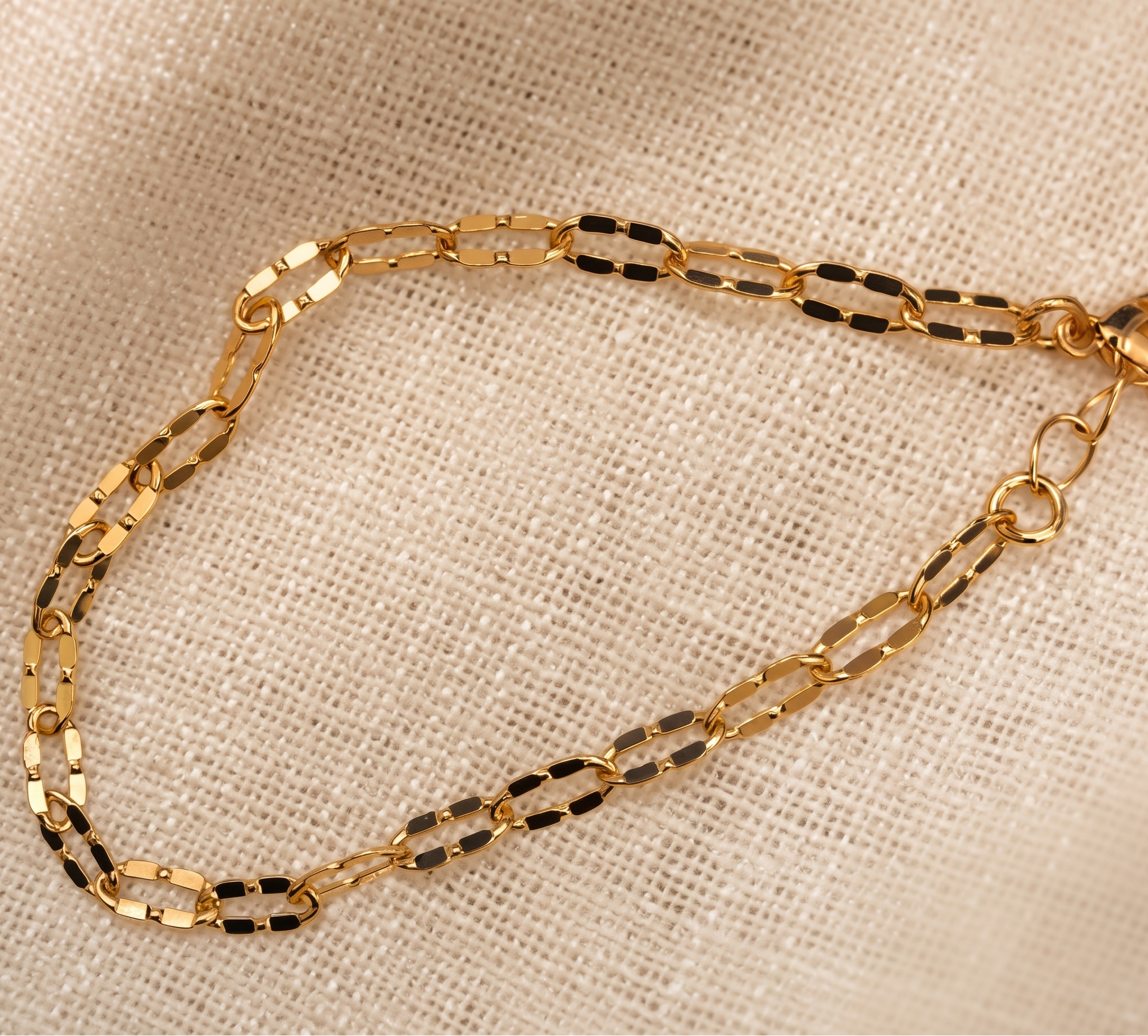 Gold chain bracelet on a beige fabric background