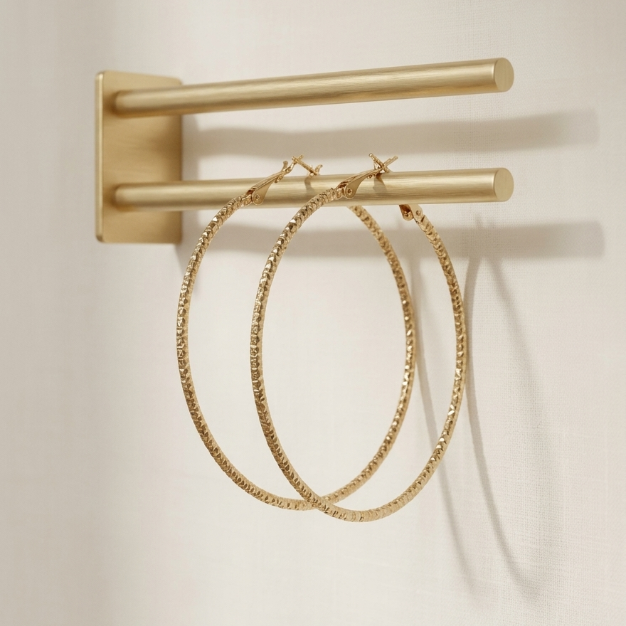 Gold hoop earrings hanging on a gold rack against a beige background