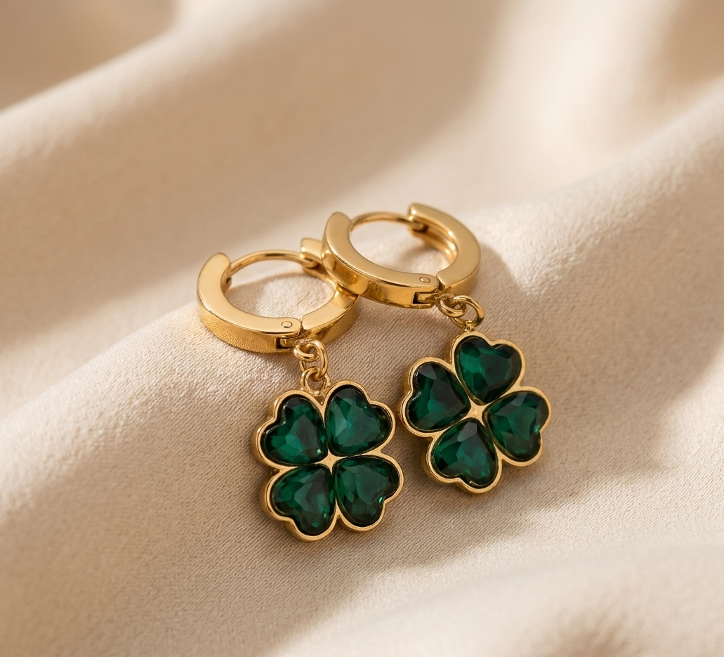 Gold earrings with green clover-shaped charms on a beige fabric background