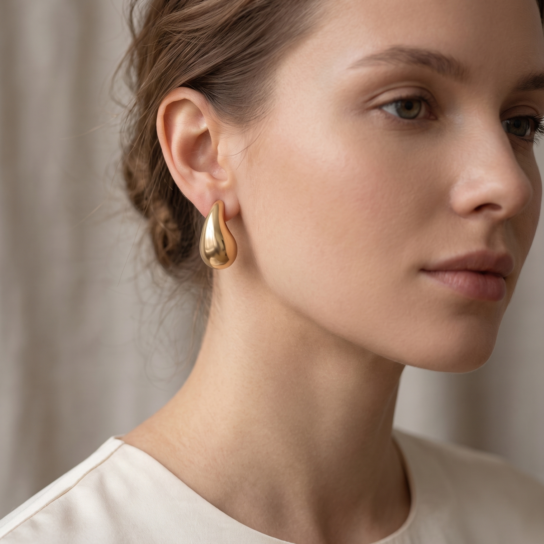 Close-up of a woman wearing gold hoop earrings with a neutral background