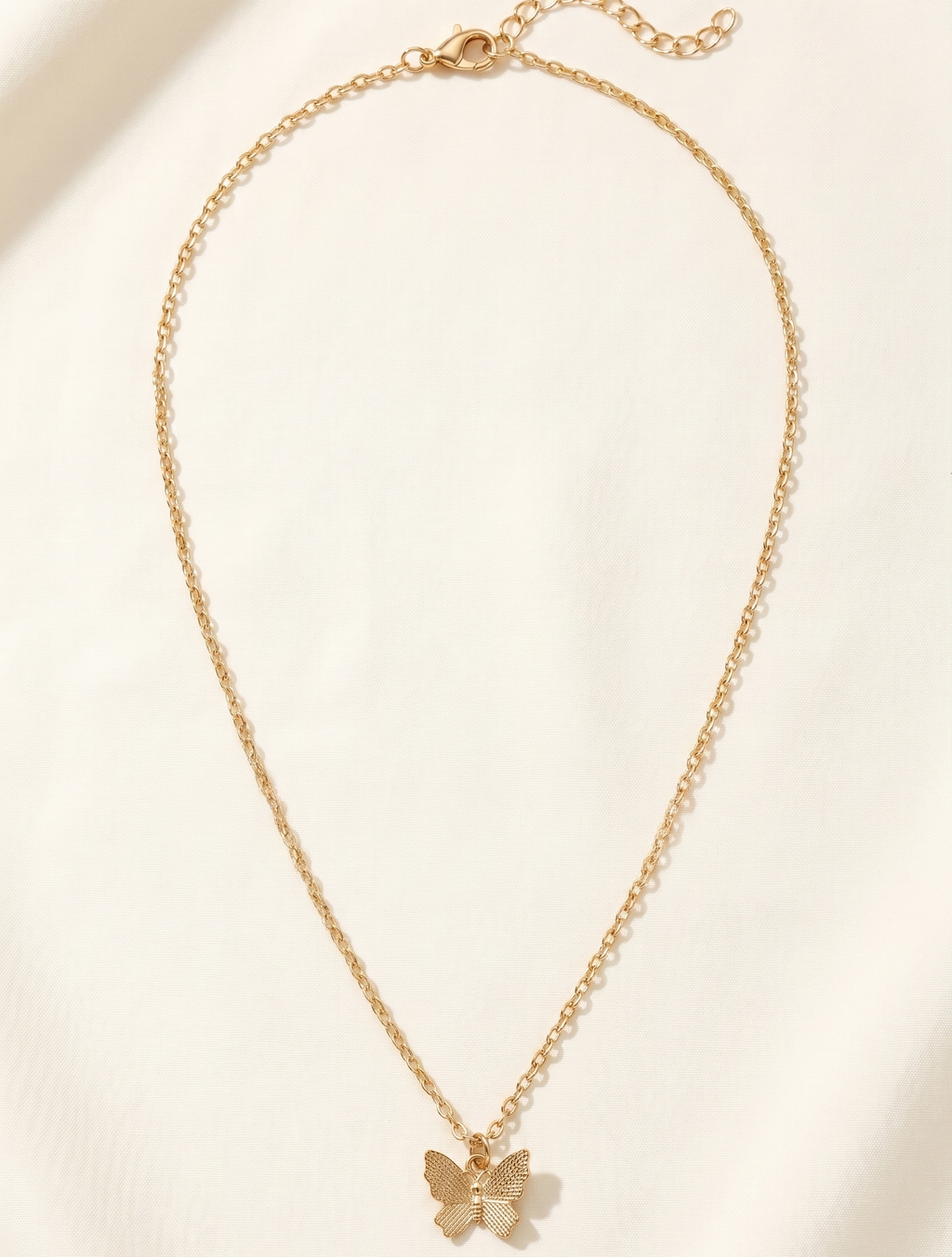 Gold butterfly necklace on a light beige background