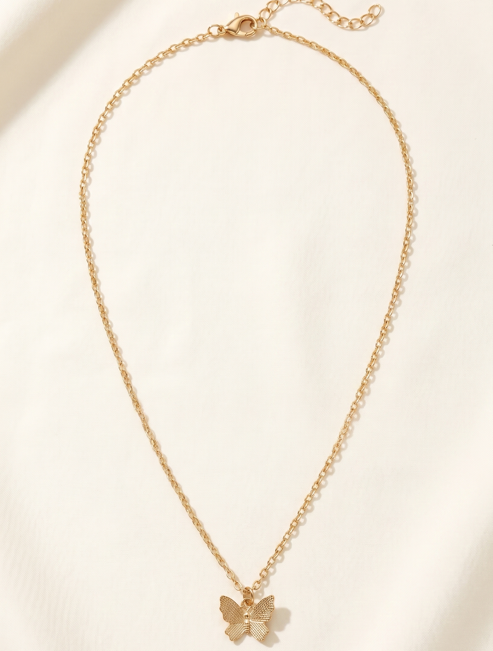Gold butterfly necklace on a light beige background