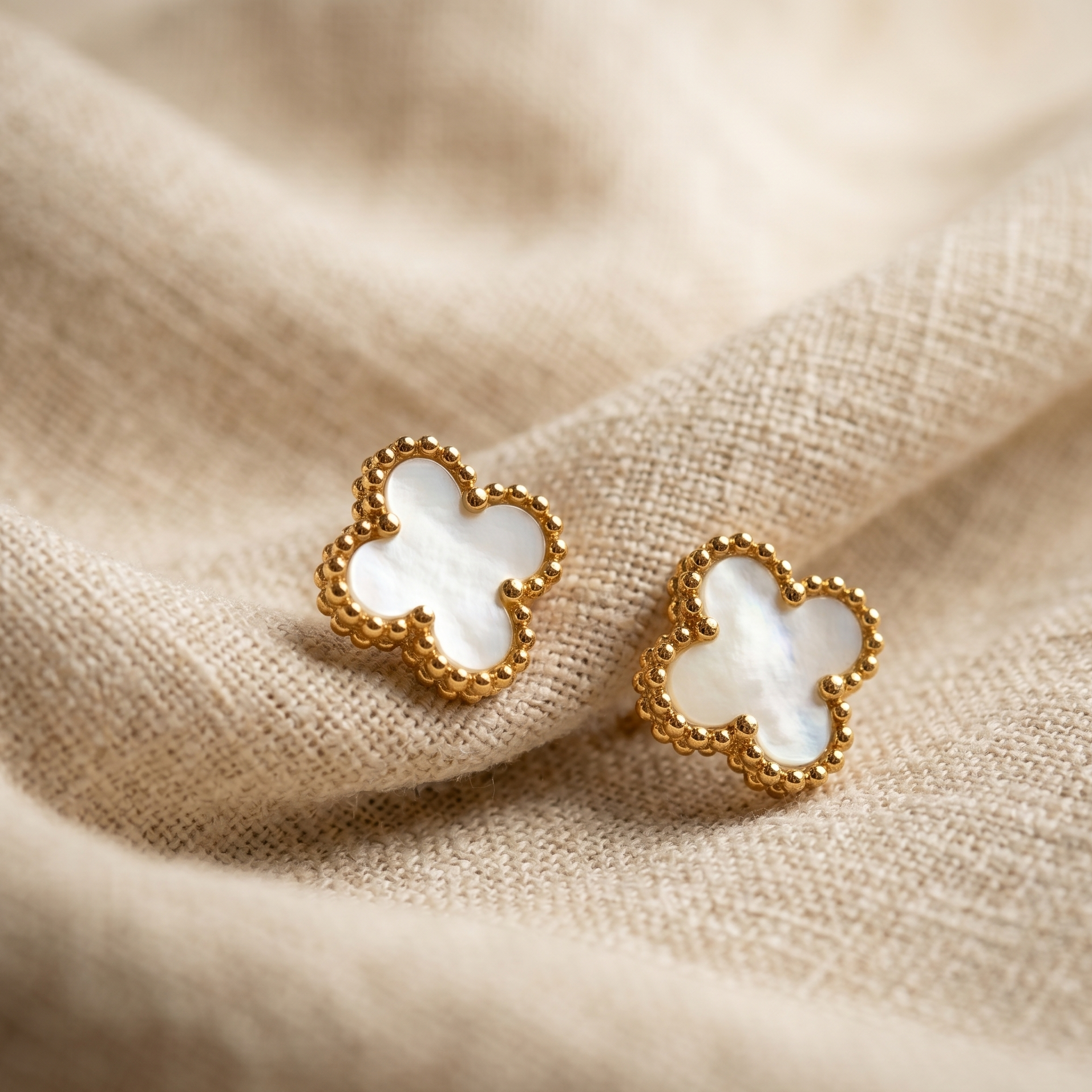Gold and white clover-shaped earrings on beige fabric