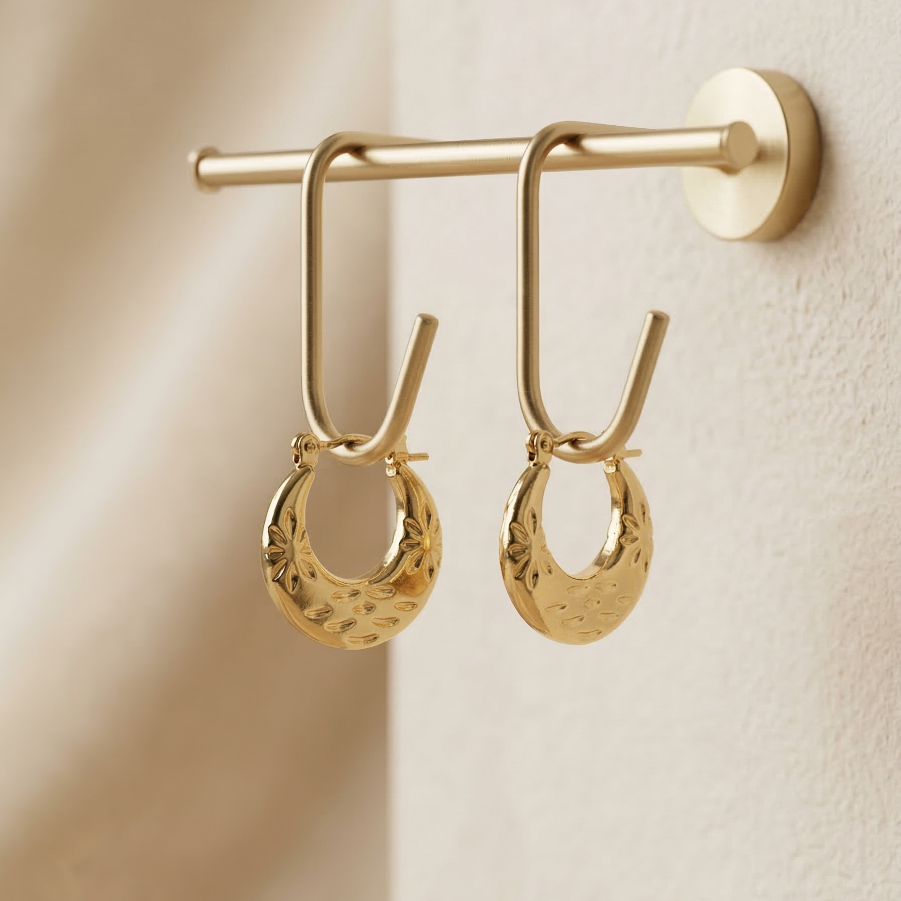 Gold hoop earrings hanging on a beige surface