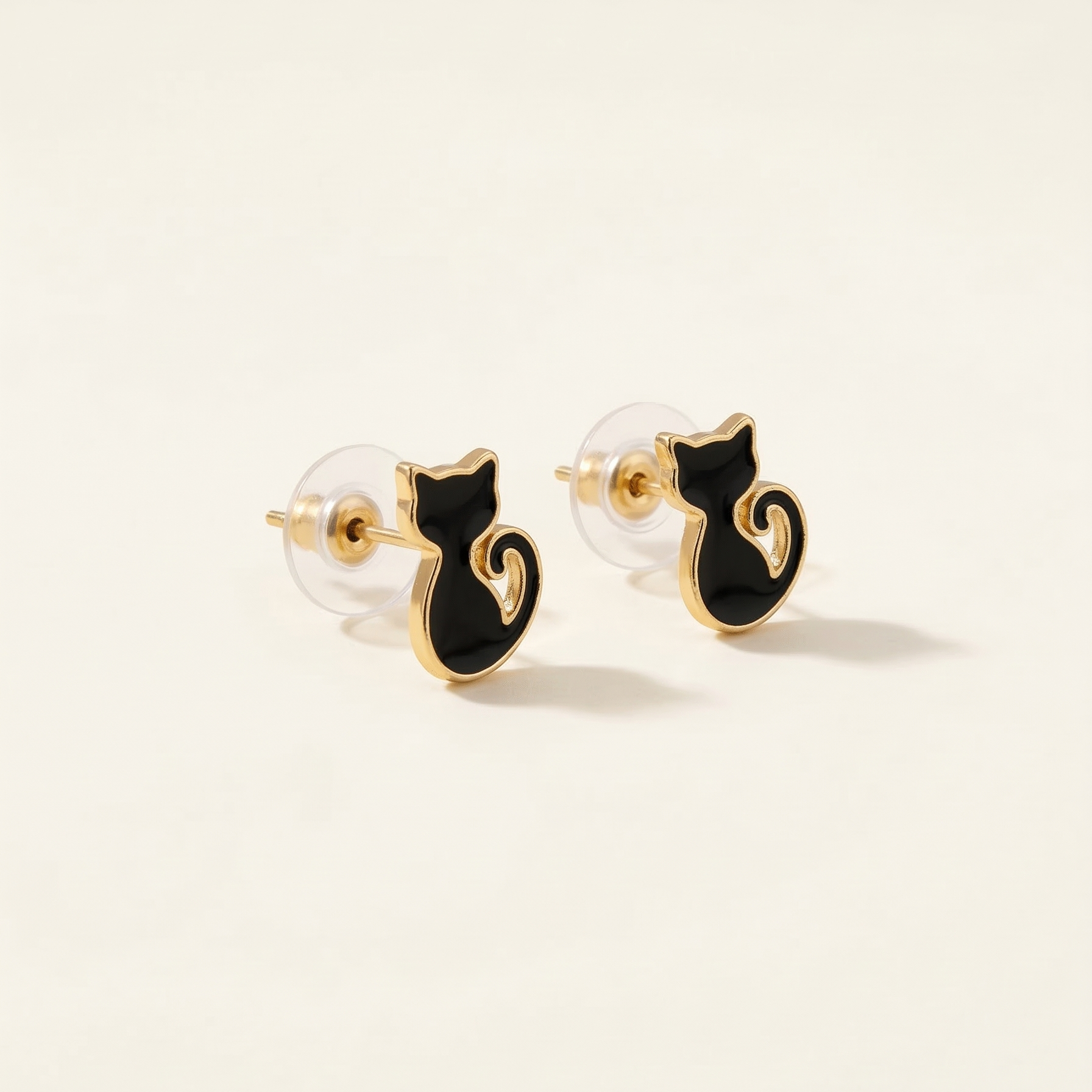 Black cat-shaped earrings with gold accents on a beige background