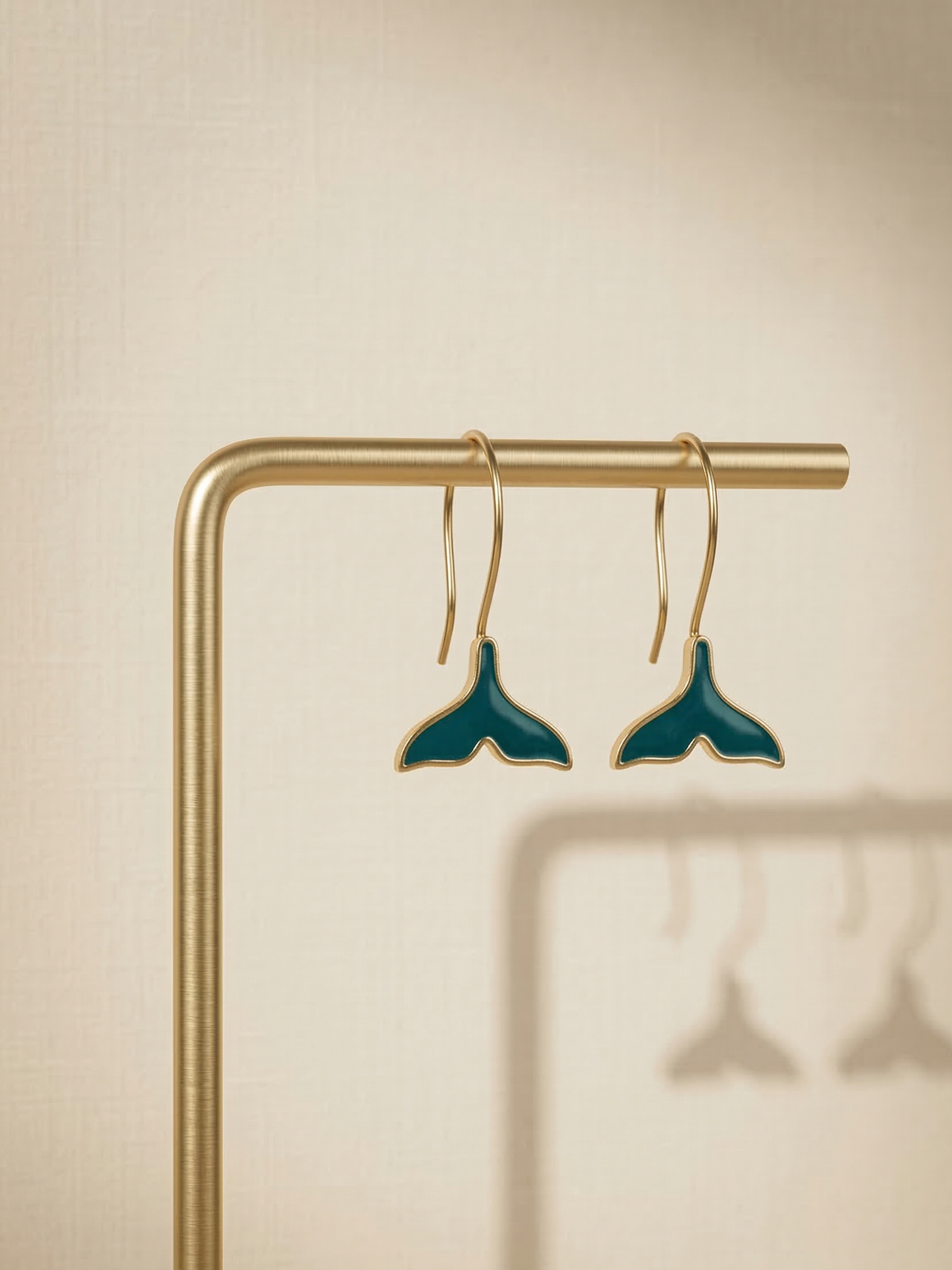 Teal whale tail earrings on a gold stand against a beige background
