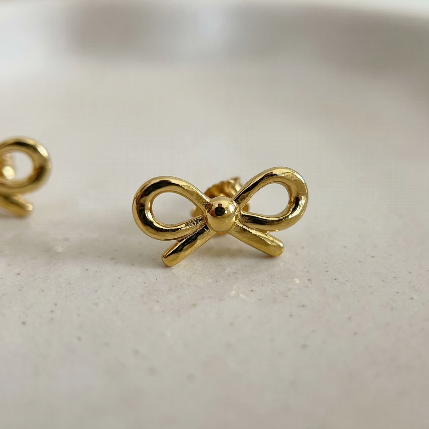 Gold bow-shaped earrings on a light background