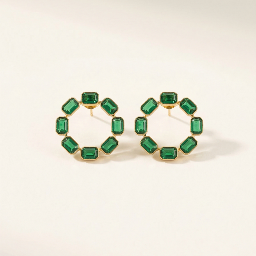 Gold hoop earrings with green gemstones on a light beige background