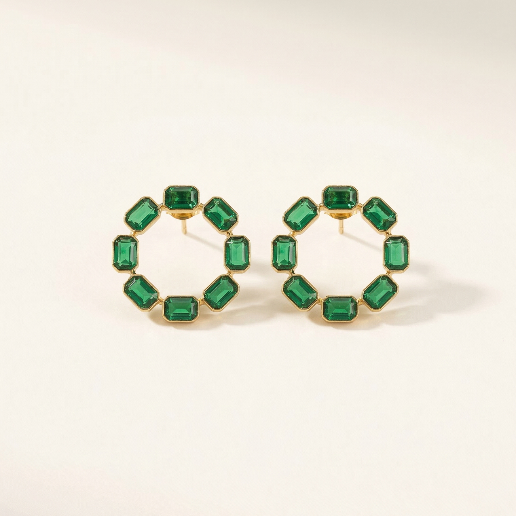 Gold hoop earrings with green gemstones on a light beige background