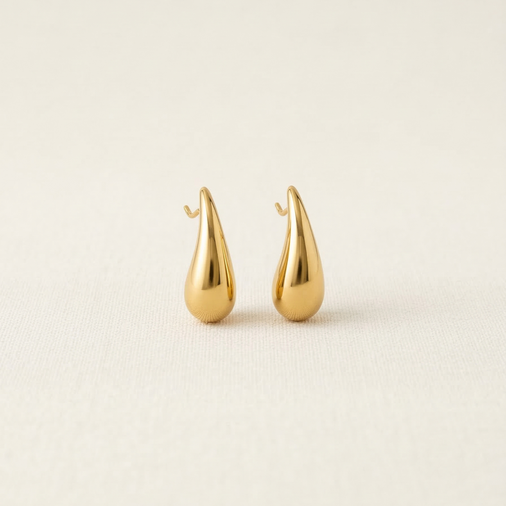 Pair of gold teardrop-shaped earrings on a beige background