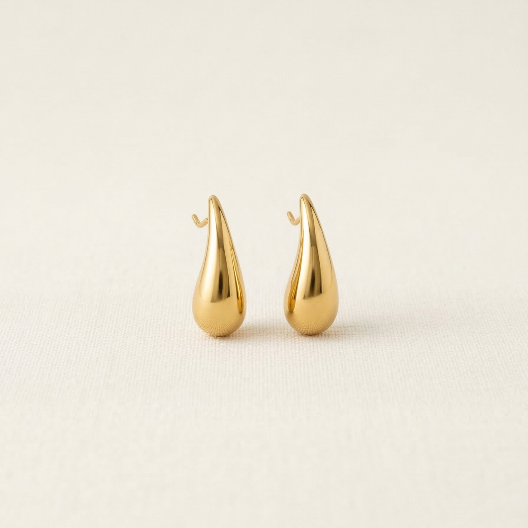 Pair of gold teardrop-shaped earrings on a beige background