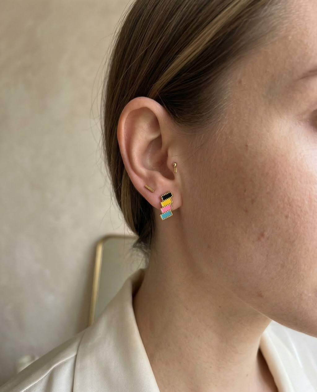 Close-up of an ear wearing colorful earrings with a neutral background