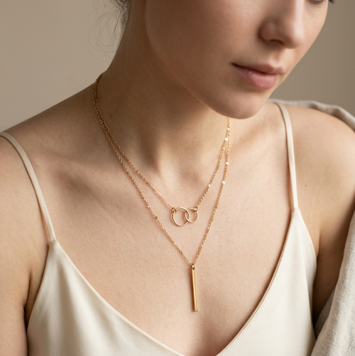 Woman wearing a gold necklace with a minimalistic design on a neutral background
