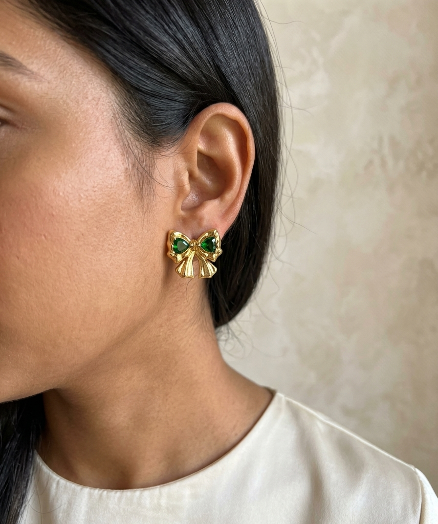 Close-up of a person wearing gold earrings with green gemstones against a neutral background