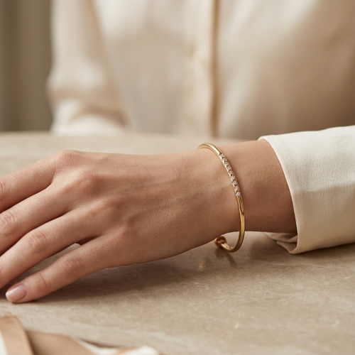 Hand wearing a gold bracelet on a table with a bowl and tissue paper.