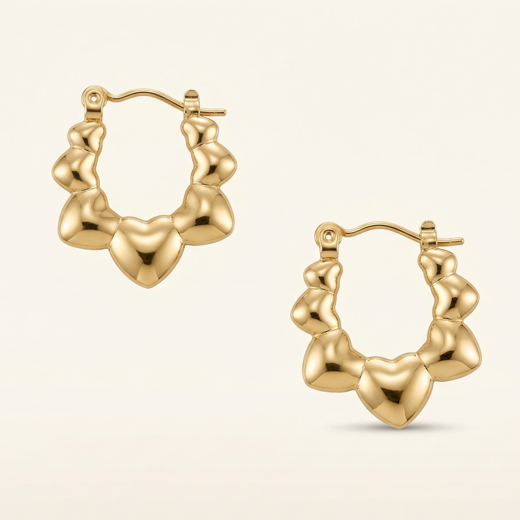 Gold hoop earrings with heart-shaped designs on a beige background