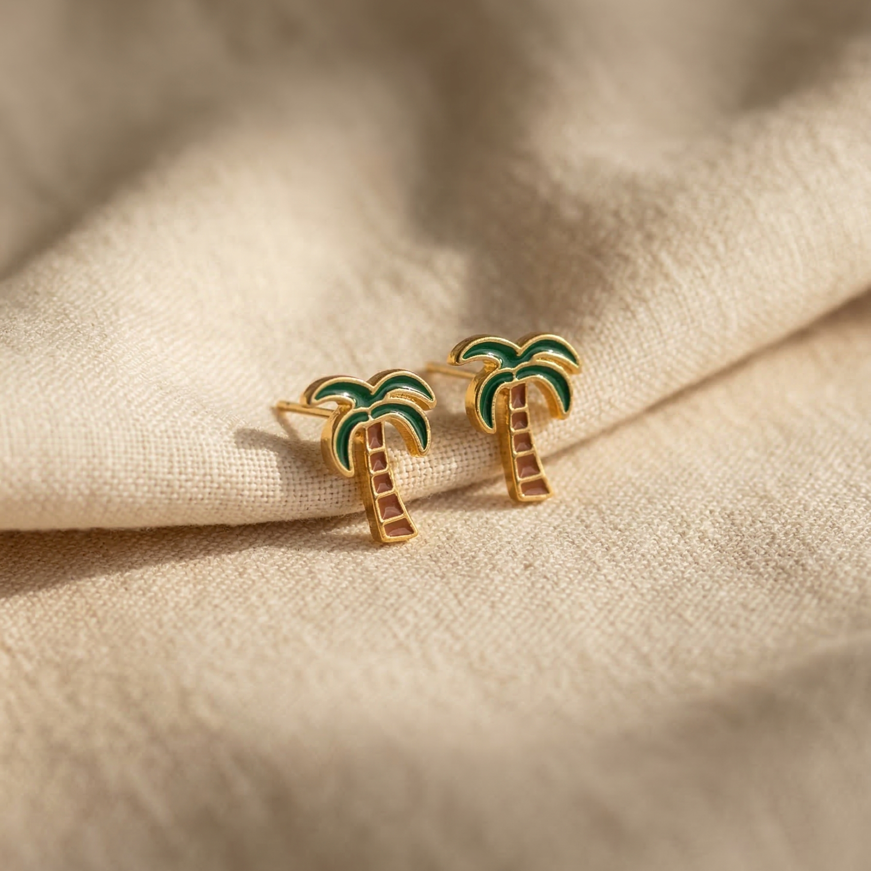 Palm tree earrings on a beige fabric background