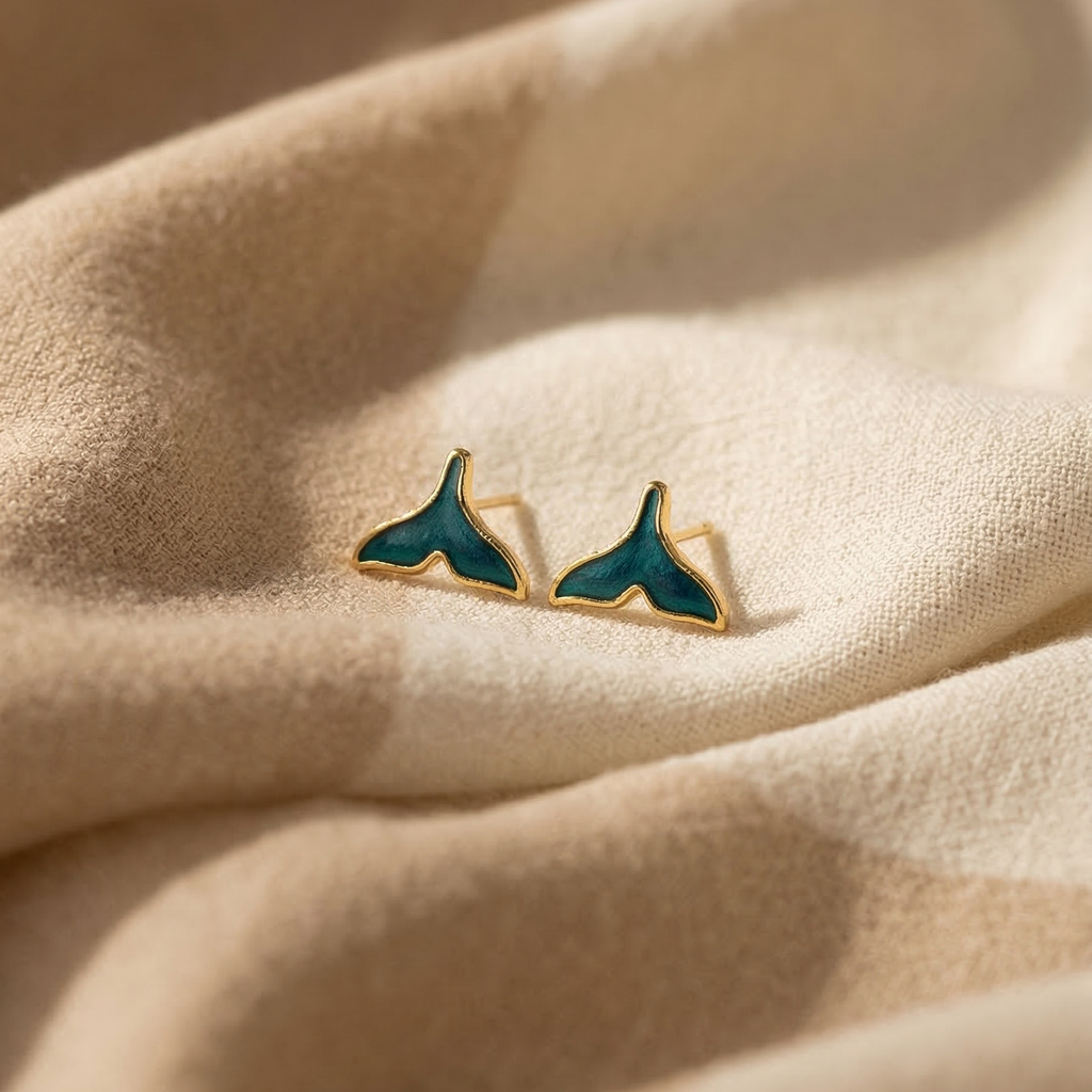 Teal whale tail earrings on beige fabric