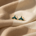 Teal whale tail earrings on beige fabric