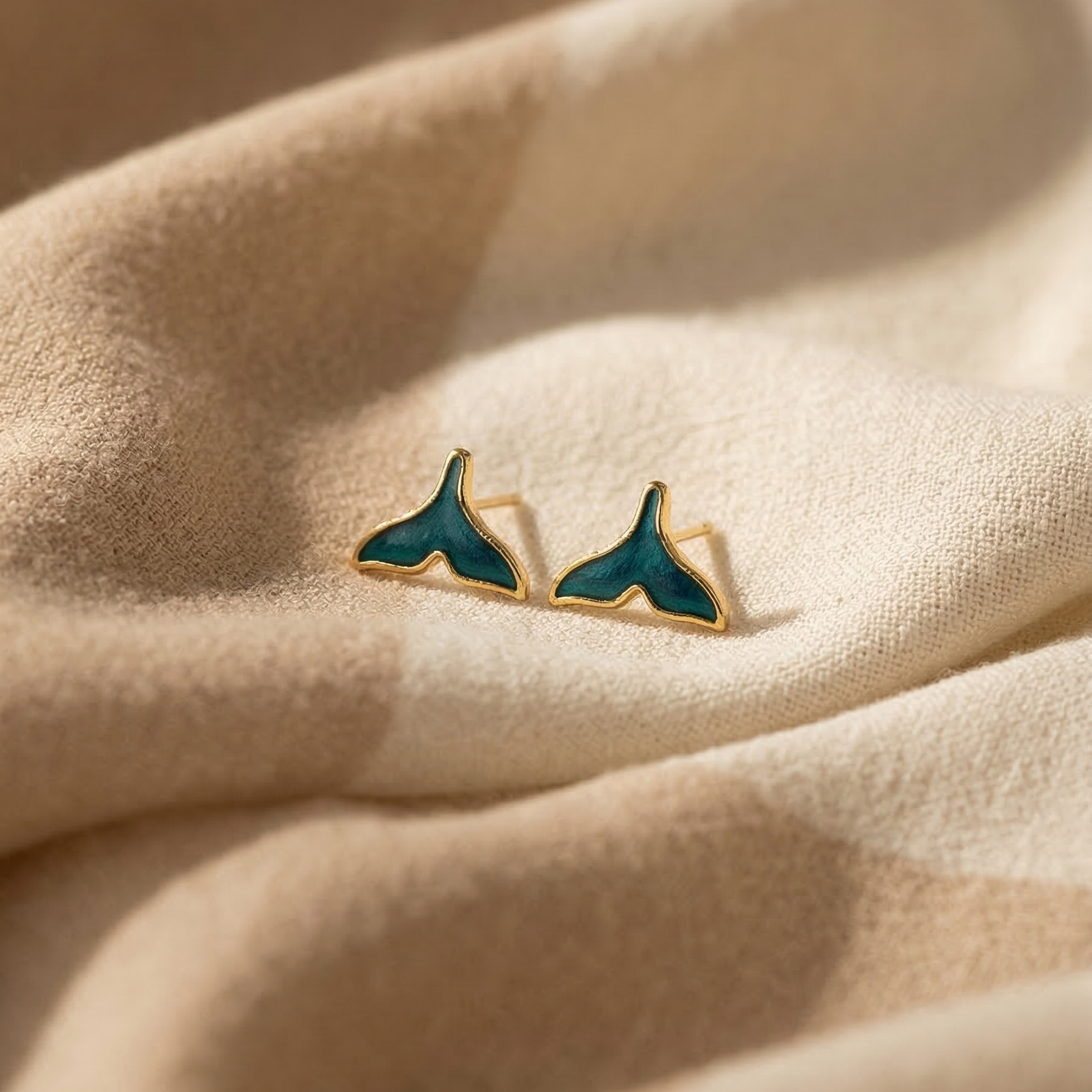Teal whale tail earrings on beige fabric