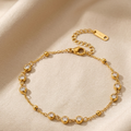 A delicate gold chain bracelet with small bead accents and clear round gemstones, displayed on a soft beige fabric background.