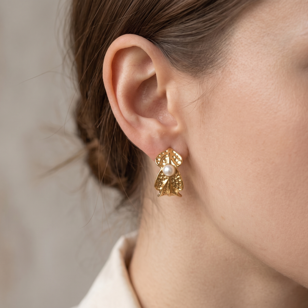 Gold earrings with a pearl detail worn by a person against a neutral background